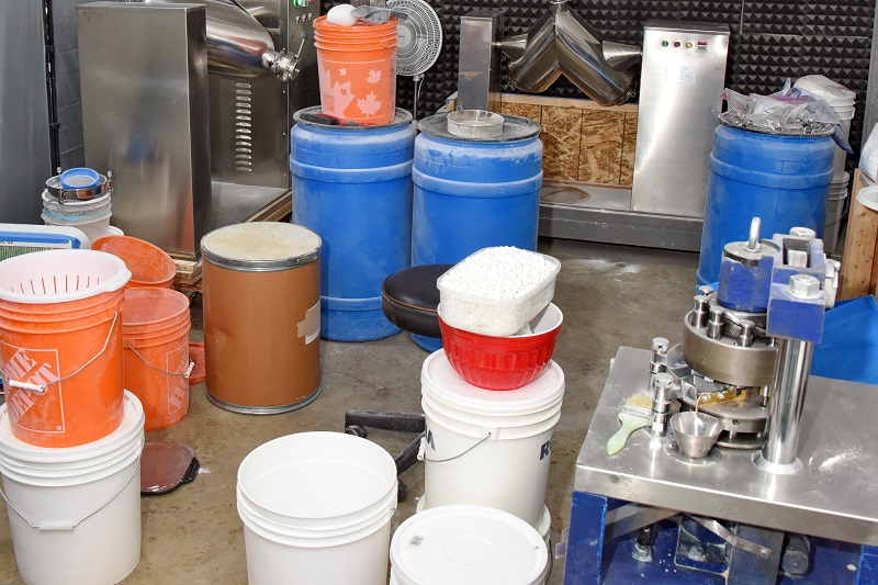 Photo of a pill press lab with mixing machines, drug powder precursor chemicals, pill pressers, and finished counterfeit pills